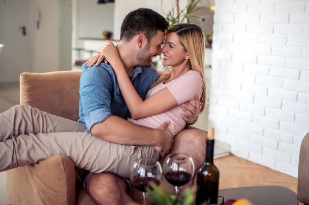 Νεαρό ζευγάρι που αγαπούν πίνοντας ένα ποτήρι κόκκινο κρασί στο σαλόνι τους. - Φωτογραφία, εικόνα