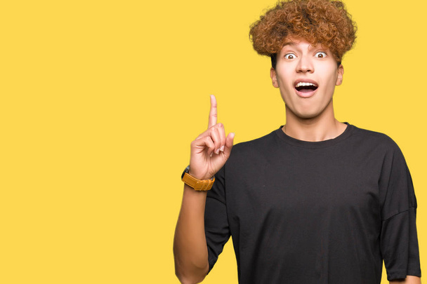 Young handsome man with afro hair wearing black t-shirt pointing finger up with successful idea. Exited and happy. Number one. - Photo, Image