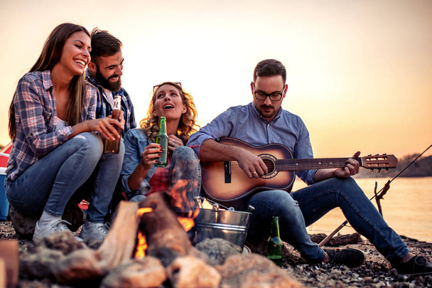 Group of cheerful friends playing  guitar and have barbecue together. - Foto, afbeelding
