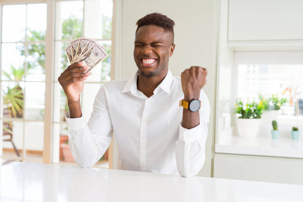 Hombre afroamericano sosteniendo billetes de cincuenta dólares gritando orgulloso y celebrando la victoria y el éxito muy emocionado, animando emoción
 - Foto, Imagen
