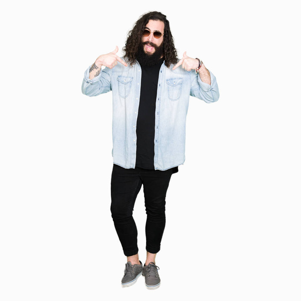 Young hipster man with long hair and beard wearing sunglasses looking confident with smile on face, pointing oneself with fingers proud and happy. - Photo, Image