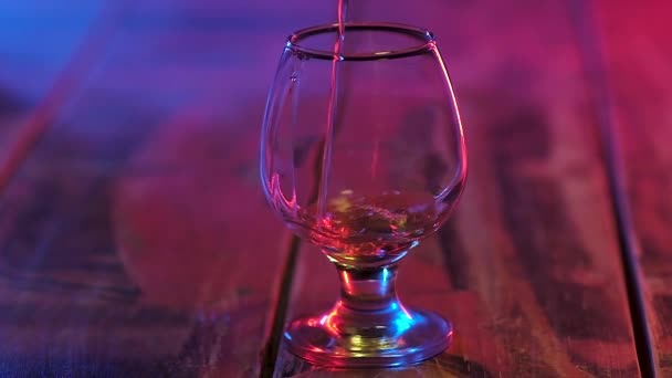 alkollü içecekler için şeffaf bir cam, çok renkli aydınlatma ahşap bir masa üzerinde duran eski güçlü konyak ince bir dere döktü. Yavaş çekim. - Video, Çekim