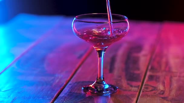in einem Glas mit einem dünnen Stiel ein Strom von rot gegossenem alkoholischen Cocktail. Zeitlupe im bunten Licht. - Filmmaterial, Video