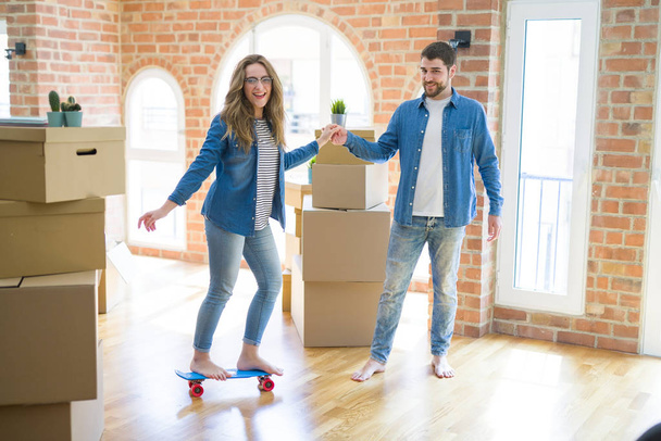 段ボール箱の周りの部屋に立ってコンピュータのラップトップを使用して若いカップルは、新しいアパートに移動するための幸せ - 写真・画像