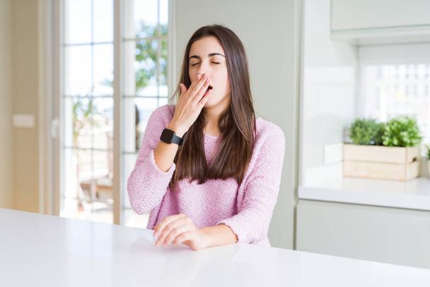 Красивая молодая женщина в розовом свитере скучает зевая усталый закрывающий рот рукой. Беспокойство и сонливость
. - Фото, изображение