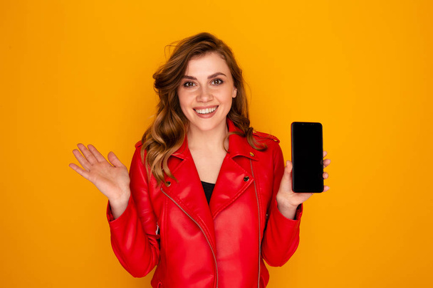 Cute female holding mobile and smiling isolated over the yellow background. - Foto, afbeelding
