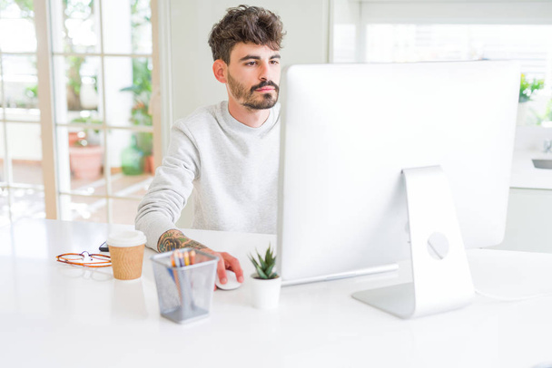 Jeune homme travaillant à l'aide d'un ordinateur avec une expression confiante sur la pensée intelligente visage grave
 - Photo, image
