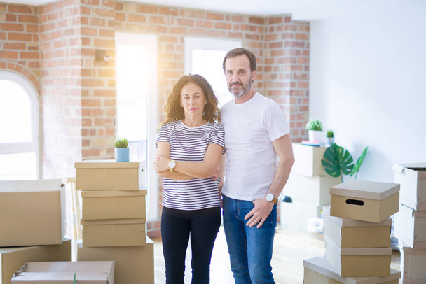 Middle age senior couple moving to a new home with boxes around with serious expression on face. Simple and natural looking at the camera. - Photo, Image