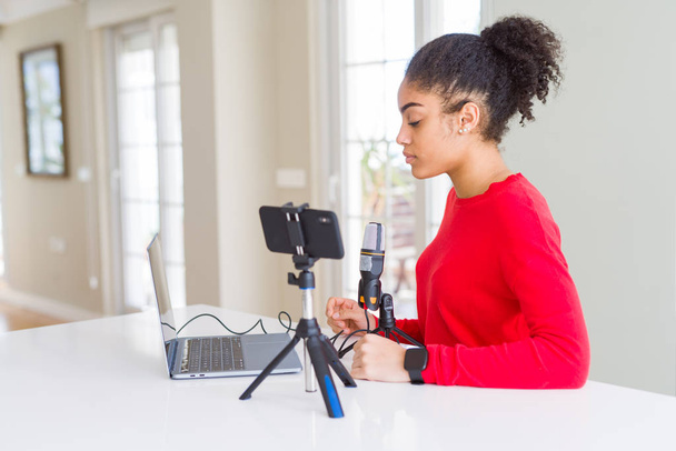Jeune femme afro-américaine faisant un appel vidéo à l'aide d'une caméra smartphone et d'un microphone regardant vers le côté, pose de profil relax avec un visage naturel avec un sourire confiant
. - Photo, image