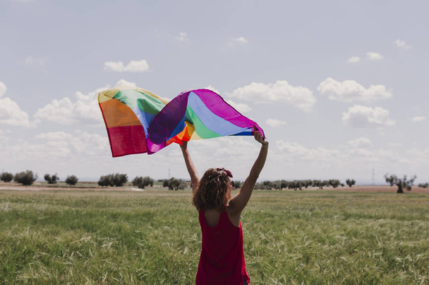 Woman holding the Gay Rainbow Flag on a green meadow outdoors. Happiness, freedom and love concept for same sex couples. LIfestyle outdoors - Valokuva, kuva