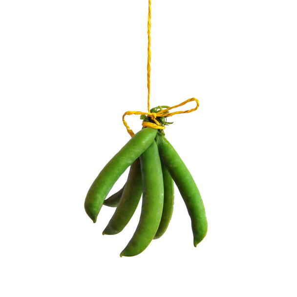 Palitos de guisantes verdes se cuelgan en una cuerda amarilla sobre un fondo blanco
. - Foto, imagen