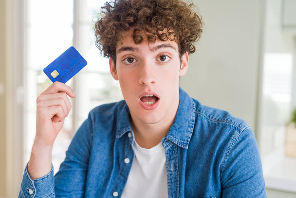Νέος άνθρωπος κρατώντας πιστωτική κάρτα φοβισμένη σε σοκ με μια έκπληξη πρόσωπο, φοβισμένος και ενθουσιασμένος με την έκφραση του φόβου - Φωτογραφία, εικόνα