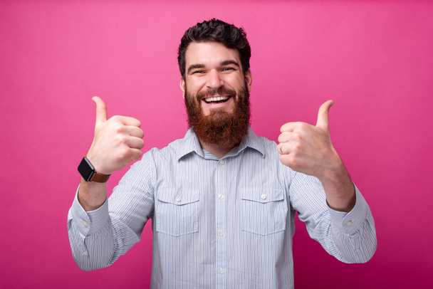 Веселий бородатий чоловік у випадковому вигляді показує великі пальці вгору жест
 - Фото, зображення