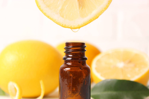 Eine Flasche ätherisches Zitronen- und Zitronenöl auf hellem Hintergrund - Foto, Bild