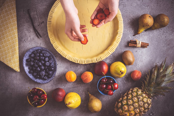 Женские руки готовят фруктовый пирог с разноцветными фруктами и свежим тестом
 - Фото, изображение