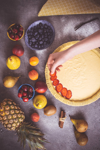 Mãos femininas preparam torta de frutas com frutas coloridas e massa fresca
 - Foto, Imagem