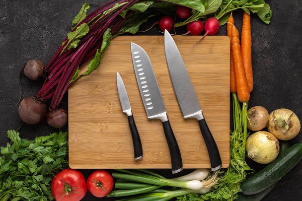 Cuchillos de cocina sobre tabla de cortar de madera con fondo de verduras frescas. Comida Cruda Vegetariana
. - Foto, Imagen