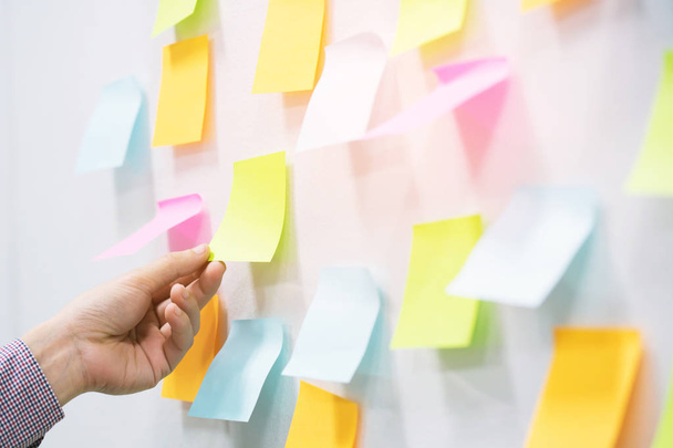 close up hand people business man post it notes in the wall at meeting room. Sticky note paper reminder schedule board. Colorful variety copy empty space. soft focus. - Photo, Image