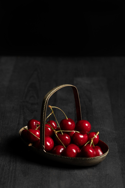 czerwony pyszne wiśnie w koszyku metalu na drewnianym ciemnym stole na białym tle na czarno - Zdjęcie, obraz