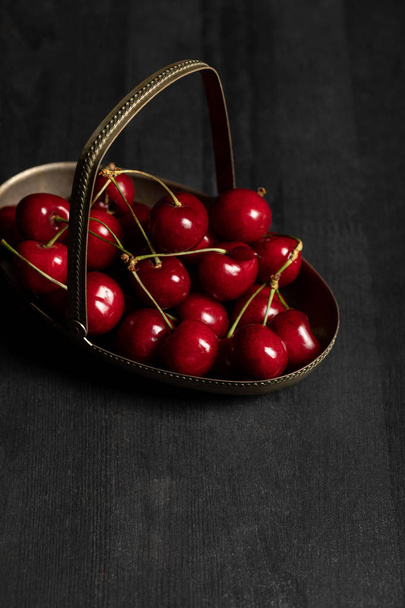 cerises rouges délicieuses dans un panier en métal sur une table sombre en bois
 - Photo, image