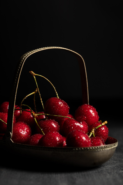 red delicious cherries with water drops in metal basket on wooden dark table isolated on black - Fotoğraf, Görsel