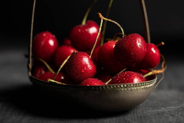 selective focus of wet red delicious cherries in metal basket on wooden dark table isolated on black - Zdjęcie, obraz