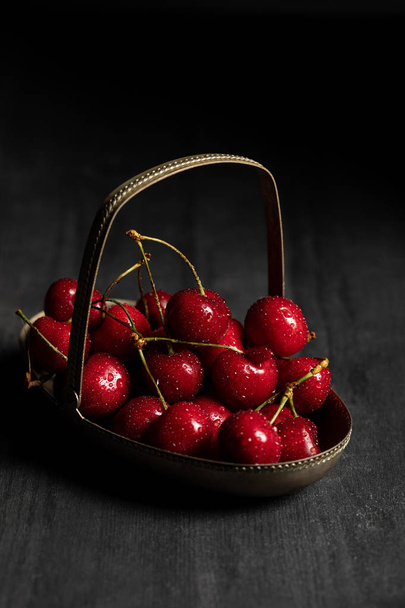 red tasty wet cherries in metal basket on wooden dark table isolated on black - Fotó, kép