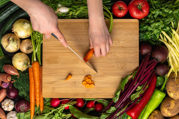 Female Hands Cutting Organic Carrot with Chef Knife on Wooden Chopping Board - Photo, Image