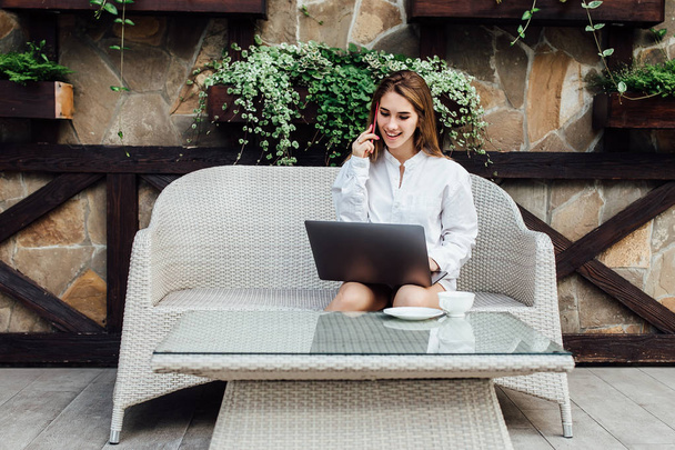 Cute woman making shopping online by gray laptop  with phone in luxury terrace. - Foto, Bild