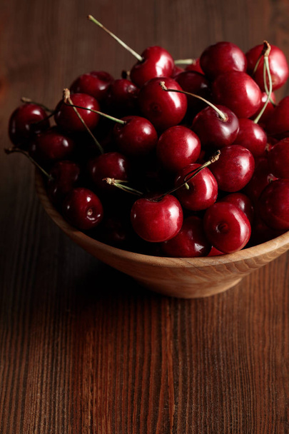 wooden bowl with red ripe cherries on wooden brown table - Fotó, kép