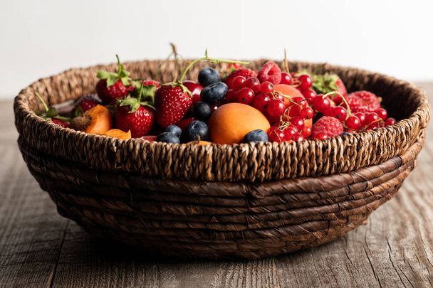 wicker basket full of seasonal berries on wooden table isolated on white - Photo, Image