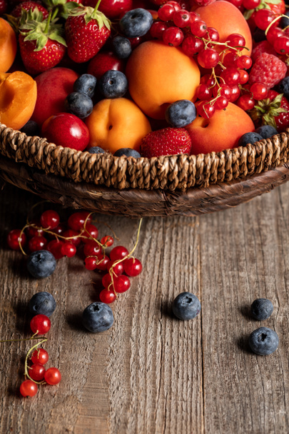 close up view of ripe berries and apricots in wicker basket on wooden table - Photo, Image