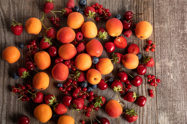 верхний вид спелых вкусных свежих ягод и абрикосов, разбросанных по деревянному столу
 - Фото, изображение