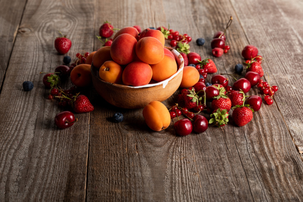 ripe delicious seasonal berries scattered around bowl with apricots on wooden table  - Photo, image
