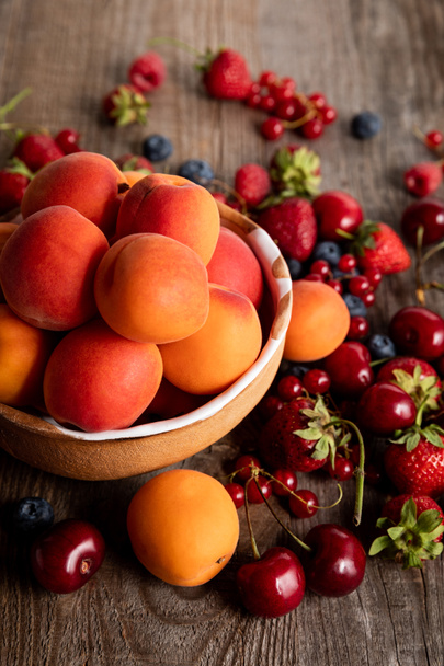 herkullisia kauden marjoja hajallaan kulhoon tuoreilla aprikooseilla puupöydällä
  - Valokuva, kuva