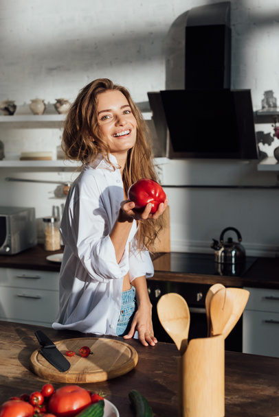 laughing young woman in white shirt holding tomato in kitchen - Valokuva, kuva