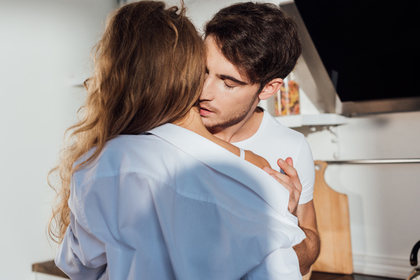 man undressing sexy girlfriend with closed eyes in kitchen - Photo, Image
