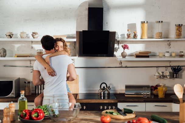 sexy pareja abrazando cerca de mesa con comida en la cocina
 - Foto, imagen