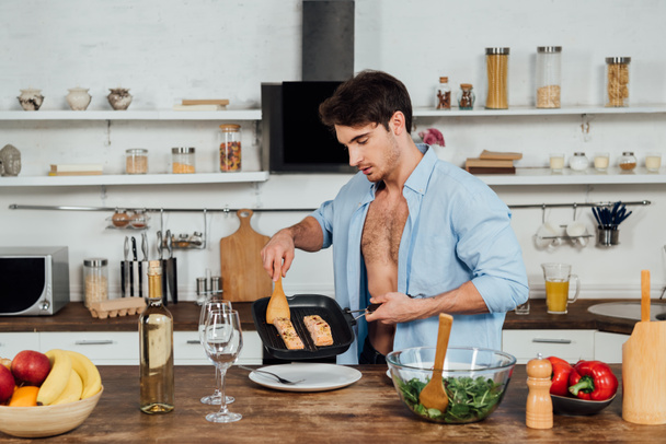 sexy hombre sosteniendo sartén con pescado en la cocina
 - Foto, imagen