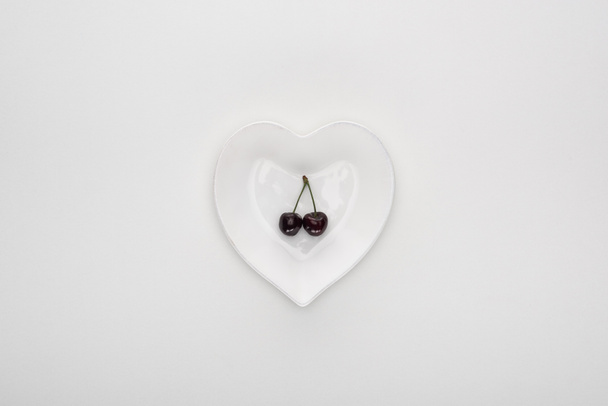 top view of red and fresh cherries on heart shaped white plate  - Foto, afbeelding