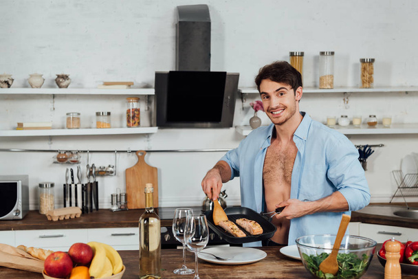 sexy smiling man holding frying pan with fish in kitchen - Foto, immagini