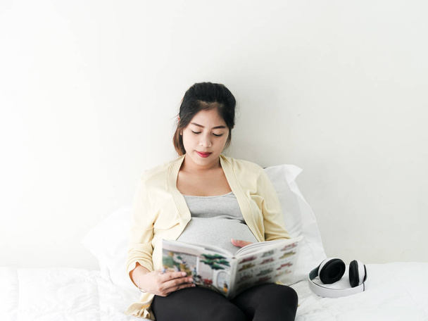Happy Asian pregnant woman reading a book on bed, lifestyle conc - Zdjęcie, obraz