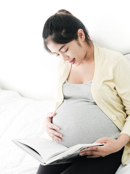 Happy Asian pregnant woman reading a book on bed, lifestyle conc - Photo, image
