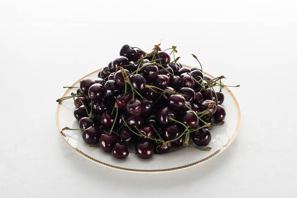 ripe, fresh and sweet cherries on plate on white background  - Фото, изображение