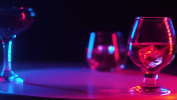 bicchiere di vetro di diverse forme con versato in loro bevande alcoliche cognac, whisky, cocktail, cubetti freddi ghiaccio trasparente filatura su un supporto di legno rotante. Illuminazione multicolore. Da vicino.
. - Filmati, video