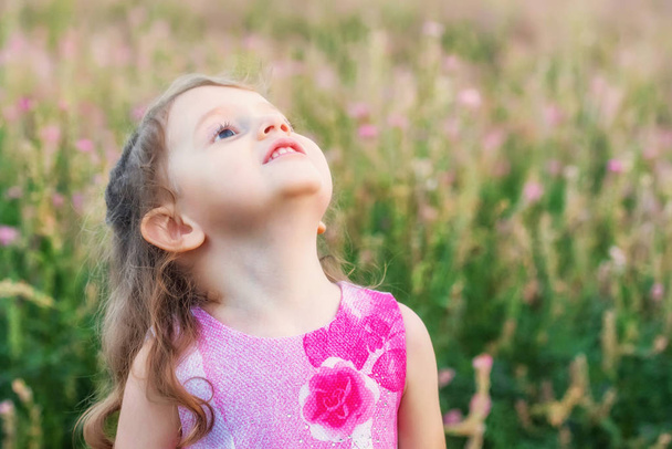 Carino sorridente bambina guarda all'aperto in campo verde. Ritratto bambino
 - Foto, immagini