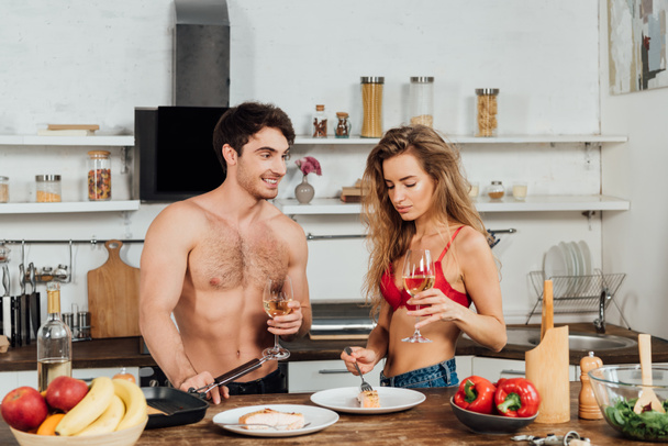 sexy couple standing near table with food and holding wine glasses - Photo, Image
