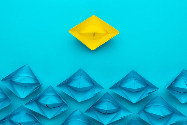 Yellow paper ship out of the crowd concept over blue background - Foto, afbeelding