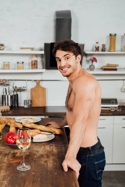 usměvavý svalnatý muž stojící blízko stolu s jídlem v kuchyni - Fotografie, Obrázek