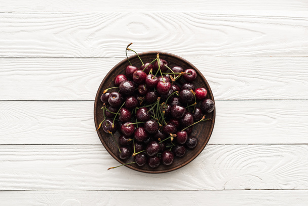 top view of fresh, sweet and wet cherries on plate on wooden background  - Photo, Image